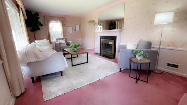 carpeted living area with a wainscoted wall, visible vents, wallpapered walls, and a fireplace with flush hearth