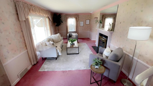 living room featuring visible vents, a fireplace with flush hearth, wainscoting, and wallpapered walls