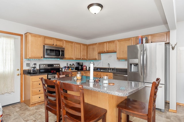 kitchen with sink, stainless steel appliances, a center island, a kitchen bar, and dark stone counters