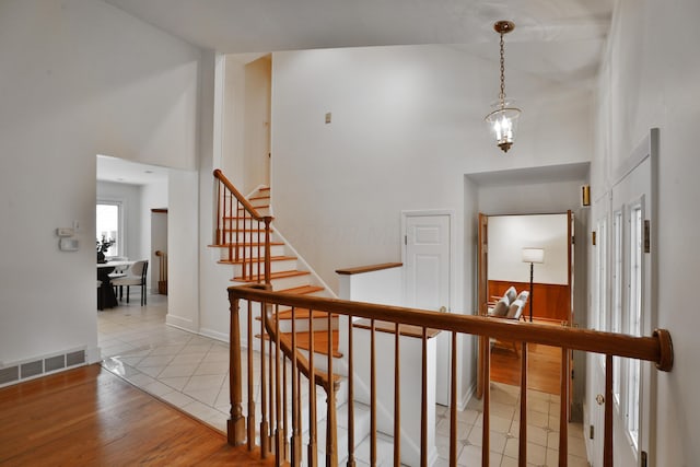 staircase with baseboards, a high ceiling, visible vents, and wood finished floors