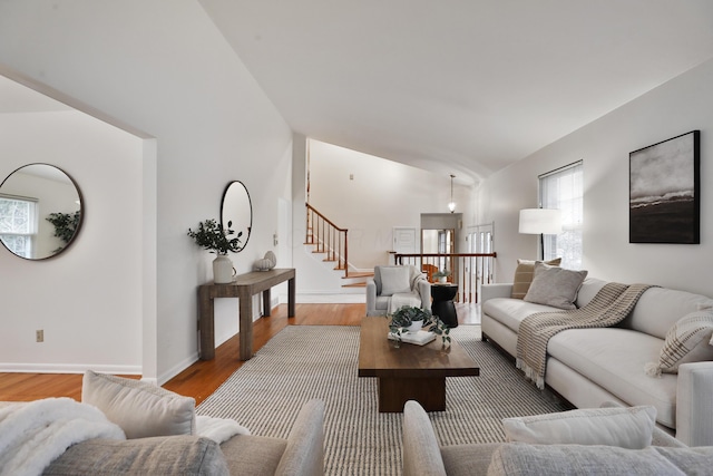 living area featuring stairs, baseboards, vaulted ceiling, and wood finished floors