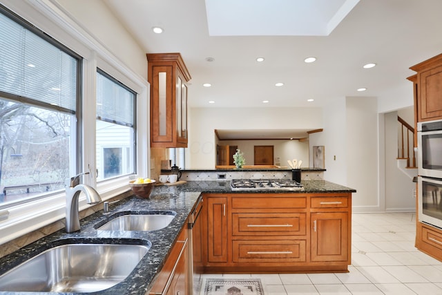 kitchen featuring recessed lighting, a sink, appliances with stainless steel finishes, brown cabinetry, and dark stone countertops