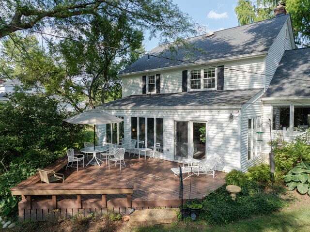 back of property featuring outdoor dining space, a chimney, roof with shingles, and a wooden deck