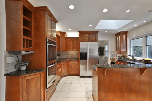 kitchen featuring light tile patterned floors, a skylight, a breakfast bar, a peninsula, and stainless steel appliances