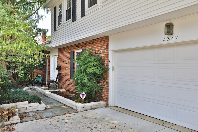 doorway to property with a garage, concrete driveway, and brick siding