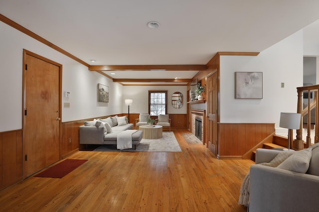 living room with a glass covered fireplace, a wainscoted wall, stairs, crown molding, and light wood-type flooring