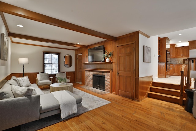 living room featuring a wainscoted wall, a fireplace, beam ceiling, and light wood-style floors