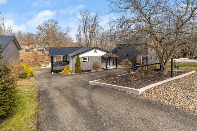 view of front facade featuring driveway, stone siding, and metal roof