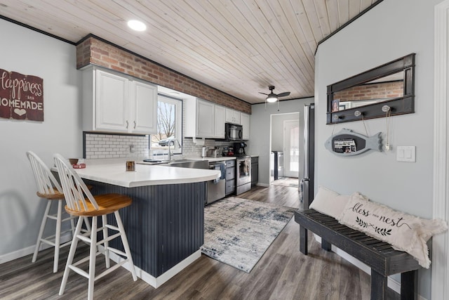 kitchen with tasteful backsplash, appliances with stainless steel finishes, white cabinetry, wooden ceiling, and a kitchen bar