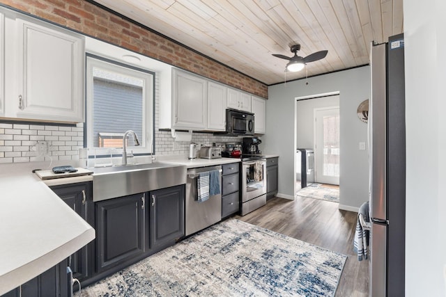 kitchen featuring brick wall, stainless steel appliances, a sink, and white cabinetry