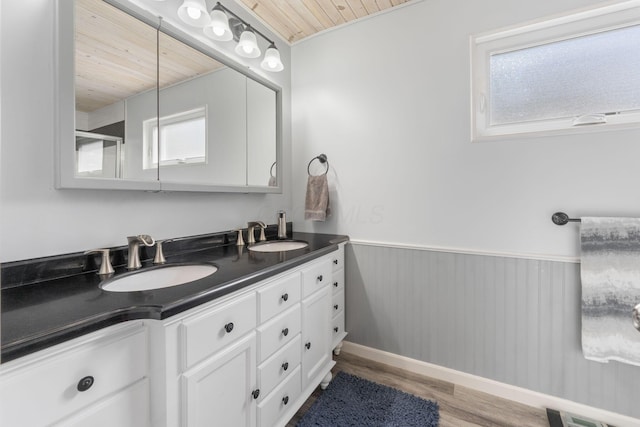 full bathroom featuring wooden ceiling, a wainscoted wall, a sink, and wood finished floors