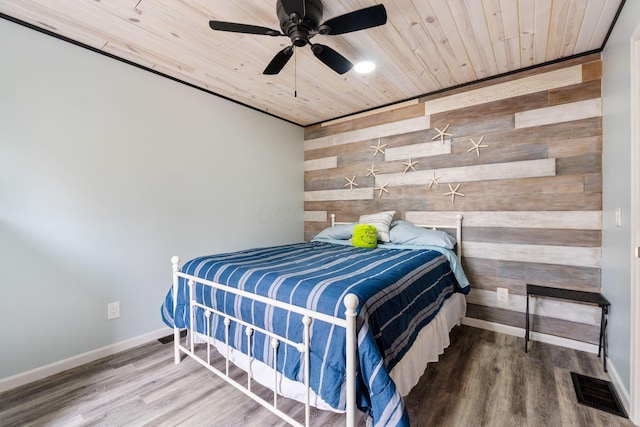 bedroom featuring visible vents, an accent wall, wood walls, wood finished floors, and wooden ceiling