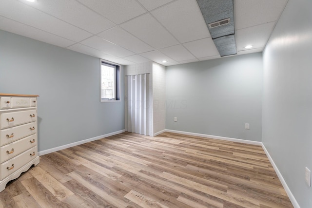 below grade area featuring light wood-type flooring, baseboards, visible vents, and a drop ceiling