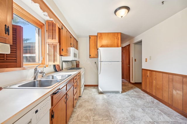 kitchen featuring wooden walls, a wainscoted wall, light countertops, white appliances, and a sink