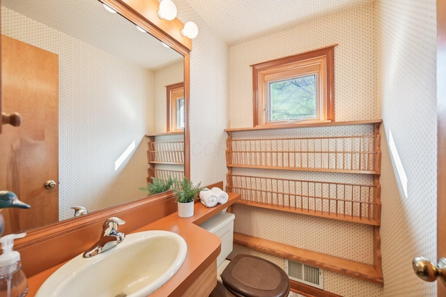 bathroom with wallpapered walls, toilet, visible vents, and a sink