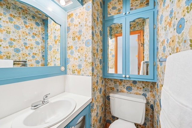 half bathroom featuring wallpapered walls, toilet, and vanity