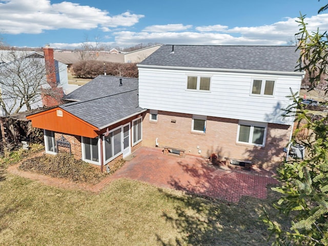 exterior space with roof with shingles, a yard, a sunroom, a patio area, and brick siding