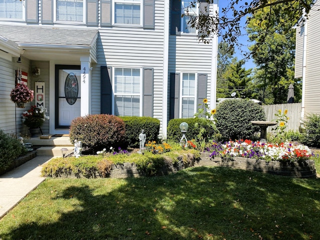 property entrance featuring a shingled roof, fence, and a lawn