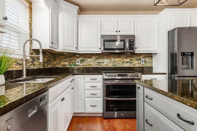 kitchen featuring light wood finished floors, tasteful backsplash, white cabinets, appliances with stainless steel finishes, and a sink