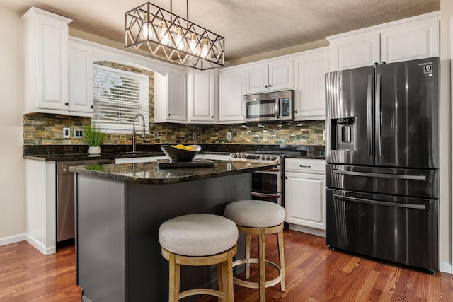 kitchen with appliances with stainless steel finishes, white cabinets, a kitchen island, a sink, and wood finished floors