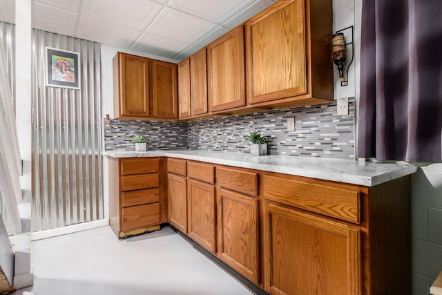 kitchen with light stone counters, brown cabinetry, and backsplash