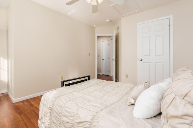 bedroom with wood finished floors, visible vents, a ceiling fan, baseboards, and attic access