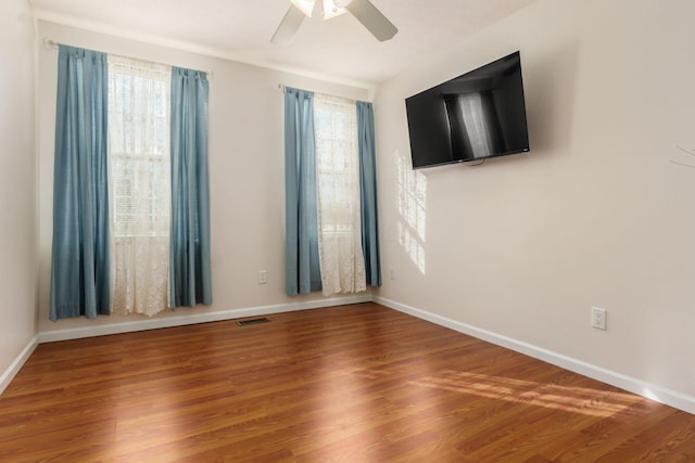 spare room with a ceiling fan, visible vents, baseboards, and wood finished floors