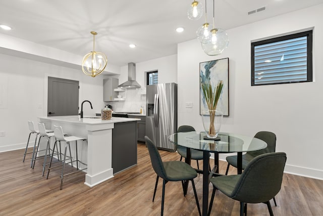 kitchen with visible vents, stainless steel fridge with ice dispenser, wall chimney exhaust hood, a kitchen island with sink, and a sink