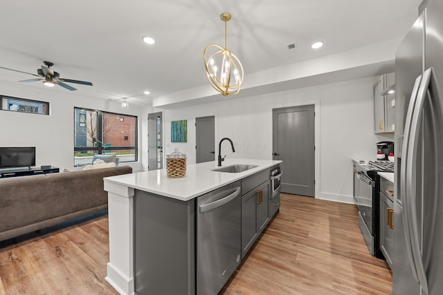 kitchen featuring stainless steel appliances, light countertops, gray cabinetry, a sink, and light wood-type flooring