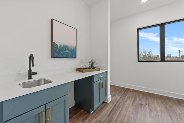 kitchen with light countertops, a sink, baseboards, and wood finished floors