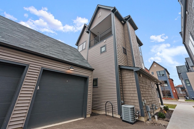 view of home's exterior with a garage, driveway, central AC unit, and roof with shingles