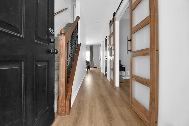 corridor featuring stairs, a barn door, light wood-type flooring, and baseboards