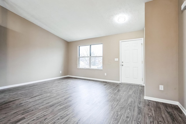 spare room featuring vaulted ceiling, dark hardwood / wood-style floors, and a textured ceiling