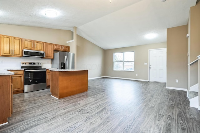 kitchen featuring lofted ceiling, stainless steel appliances, light stone counters, light hardwood / wood-style floors, and a kitchen island