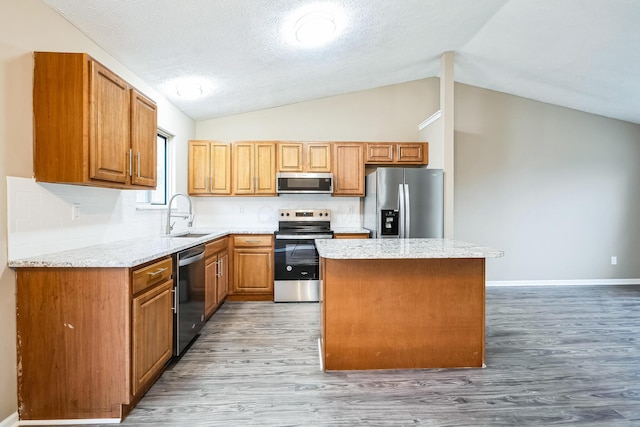 kitchen with lofted ceiling, sink, stainless steel appliances, a center island, and light hardwood / wood-style floors