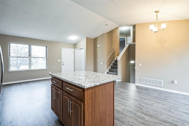 kitchen featuring vaulted ceiling, a kitchen island, dark hardwood / wood-style floors, hanging light fixtures, and light stone countertops