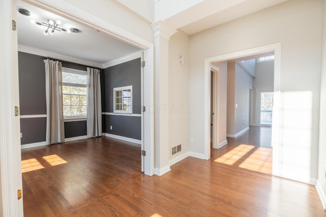 spare room with crown molding, dark wood-type flooring, and decorative columns