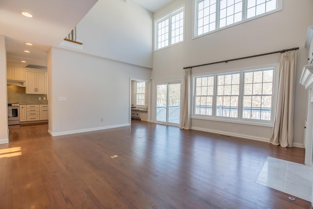 unfurnished living room featuring dark wood-type flooring, a towering ceiling, and plenty of natural light