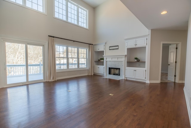 unfurnished living room featuring a high end fireplace, a towering ceiling, and dark hardwood / wood-style flooring