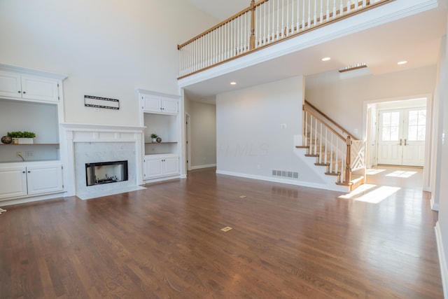 unfurnished living room featuring dark wood-type flooring, built in shelves, a high ceiling, and a fireplace