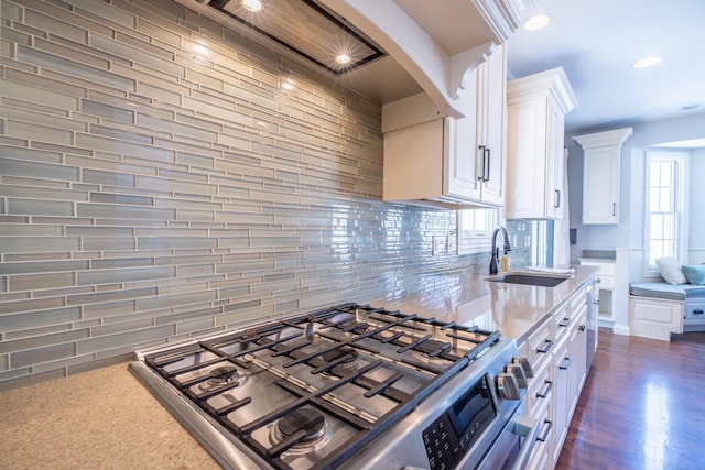 kitchen featuring dark wood-type flooring, backsplash, stainless steel gas stove, sink, and white cabinetry