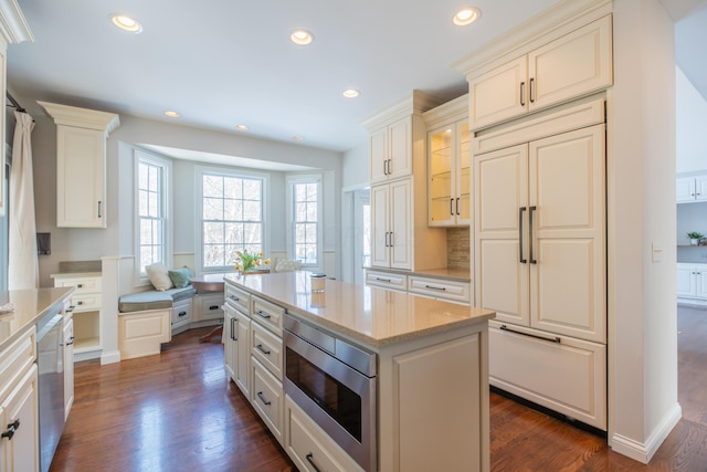 kitchen with built in appliances, a center island, dark hardwood / wood-style flooring, white cabinets, and light stone countertops