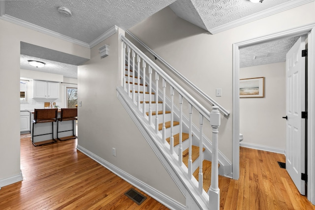 stairway with hardwood / wood-style flooring, ornamental molding, and a textured ceiling