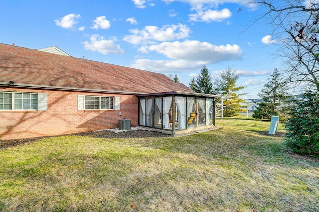 rear view of house with central air condition unit, a sunroom, and a lawn