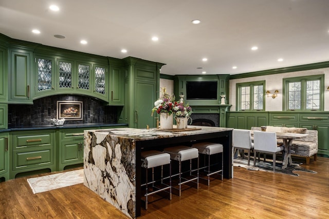 kitchen with a kitchen breakfast bar, hardwood / wood-style flooring, a center island, green cabinets, and crown molding