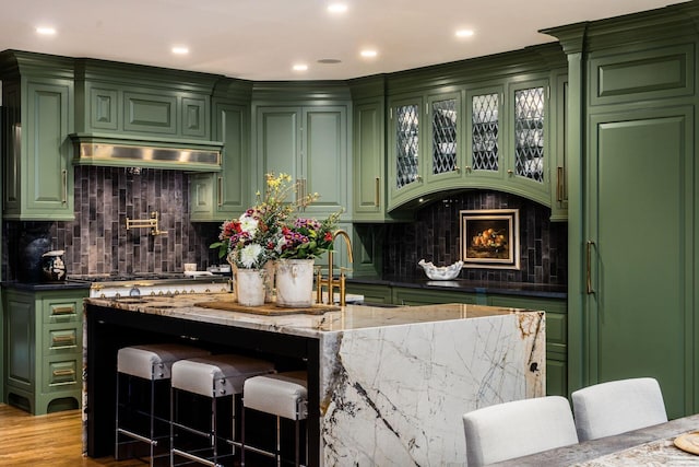 bar with decorative backsplash, ventilation hood, light stone countertops, and green cabinets