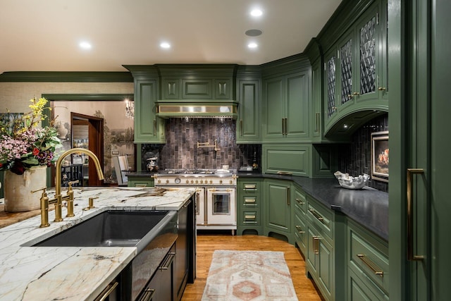 kitchen with sink, dark stone countertops, range hood, green cabinetry, and range with two ovens