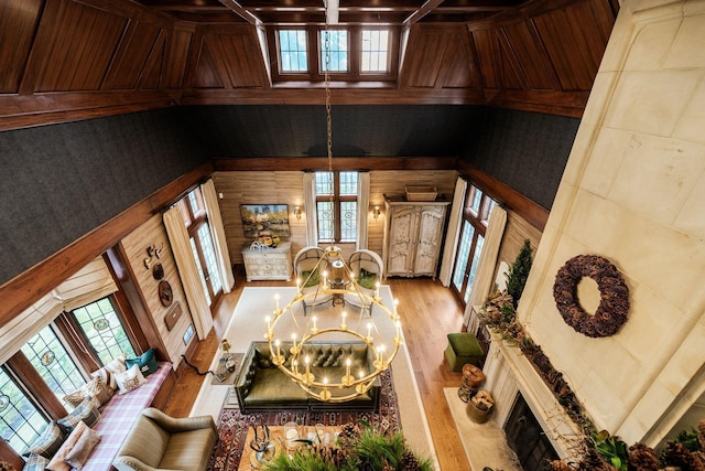 unfurnished living room featuring a towering ceiling, light wood-type flooring, a chandelier, and wood walls