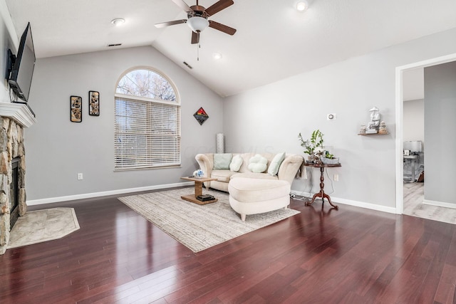 living room featuring a stone fireplace, vaulted ceiling, dark hardwood / wood-style floors, and ceiling fan