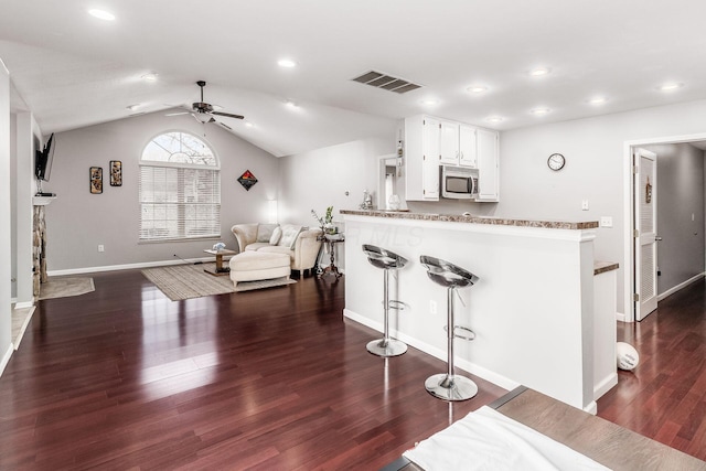 kitchen featuring dark hardwood / wood-style floors, vaulted ceiling, kitchen peninsula, and white cabinets